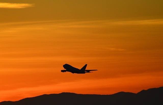 A Boeing 747 flying in the orange light of sunset over a mountain range